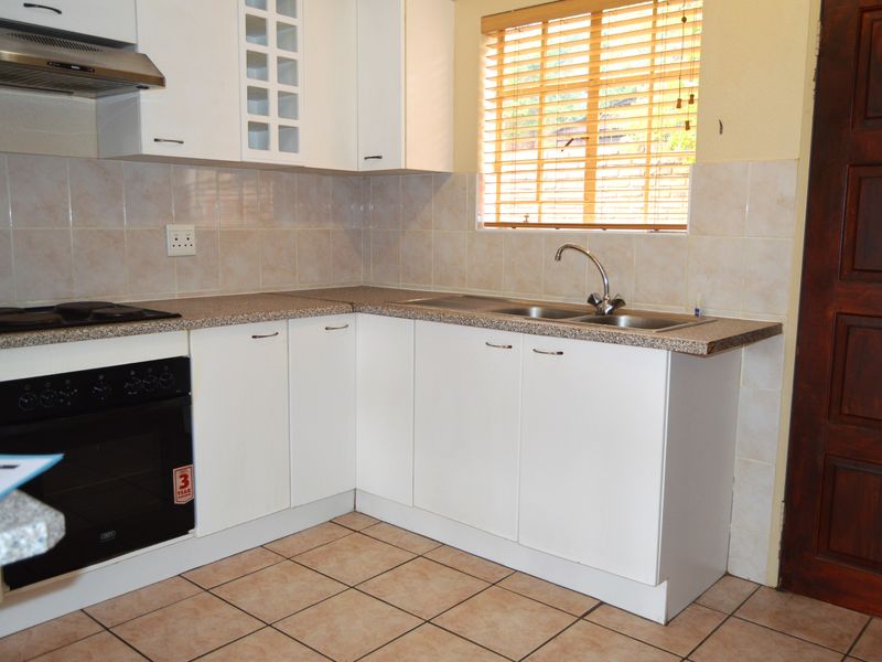 A functional kitchen featuring white cabinetry, granite-look countertops, a built-in oven with hob, extractor fan, and a double sink with tiled splashback.