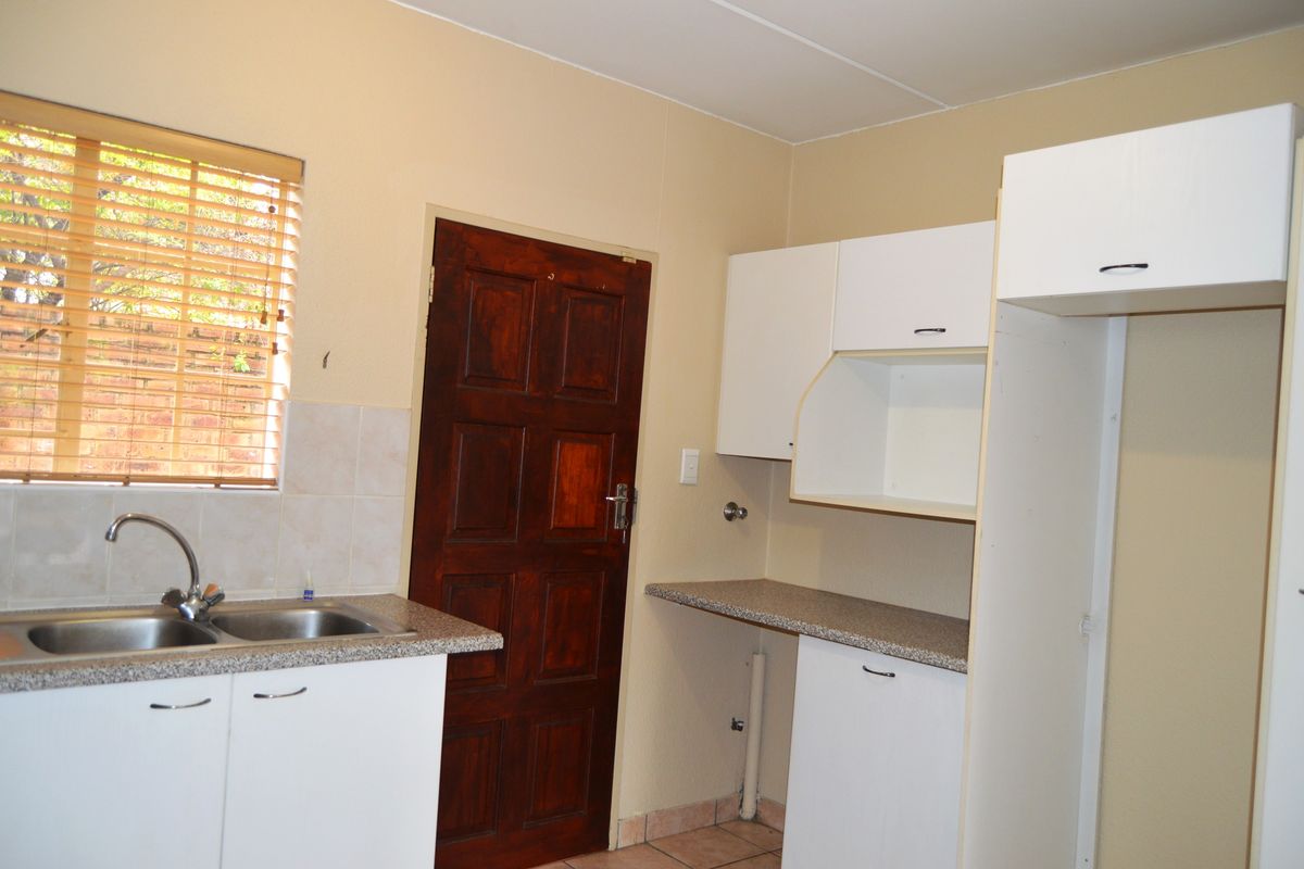 A functional kitchen area featuring white built-in cabinetry, laminate countertops, a double bowl sink, and a timber door leading to the exterior.