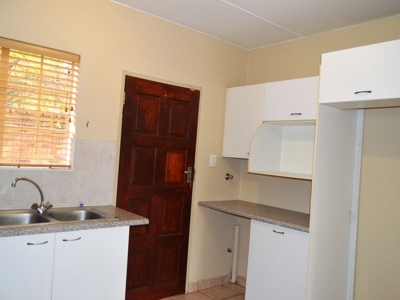 A functional kitchen area featuring white built-in cabinetry, laminate countertops, a double bowl sink, and a timber door leading to the exterior.