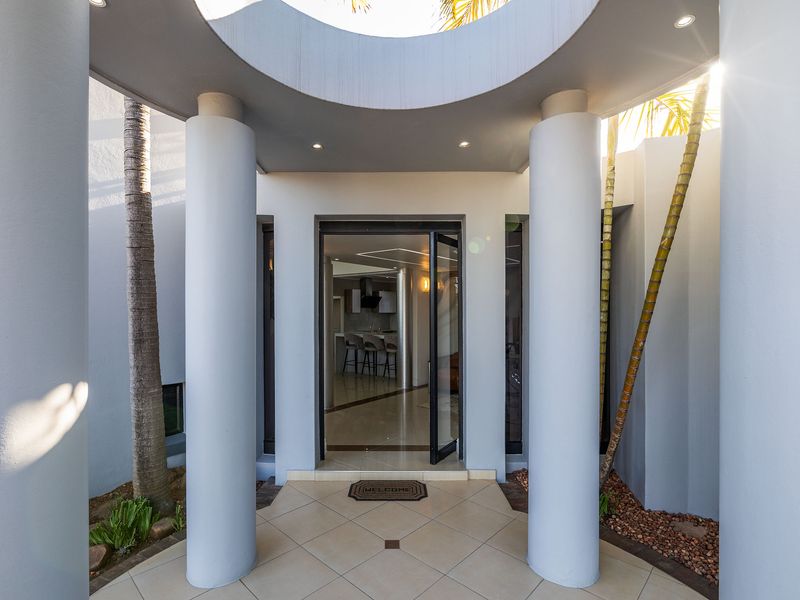 A modern entrance featuring structural columns, a unique circular ceiling cutout, and tiled flooring leading into the home.