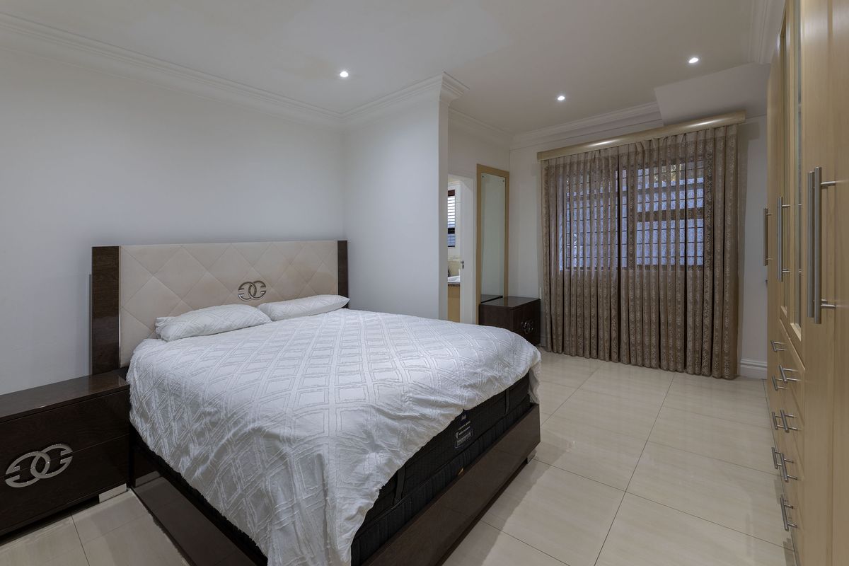 A well-maintained bedroom featuring tiled flooring, built-in cupboards, and recessed downlighting, offering a clean and neutral living space.