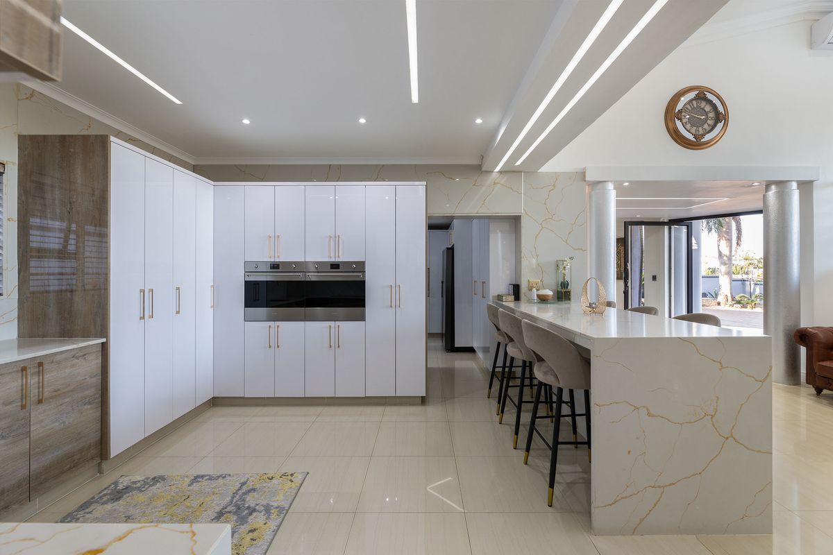 Modern kitchen featuring high-gloss cabinetry, a large stone-topped island, built-in double ovens, and elegant marble-effect wall finishes with integrated lighting.
