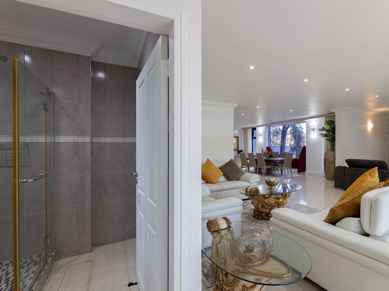 An open-plan living and dining area adjacent to a modern bathroom featuring a glass-enclosed shower with tiled finishes.