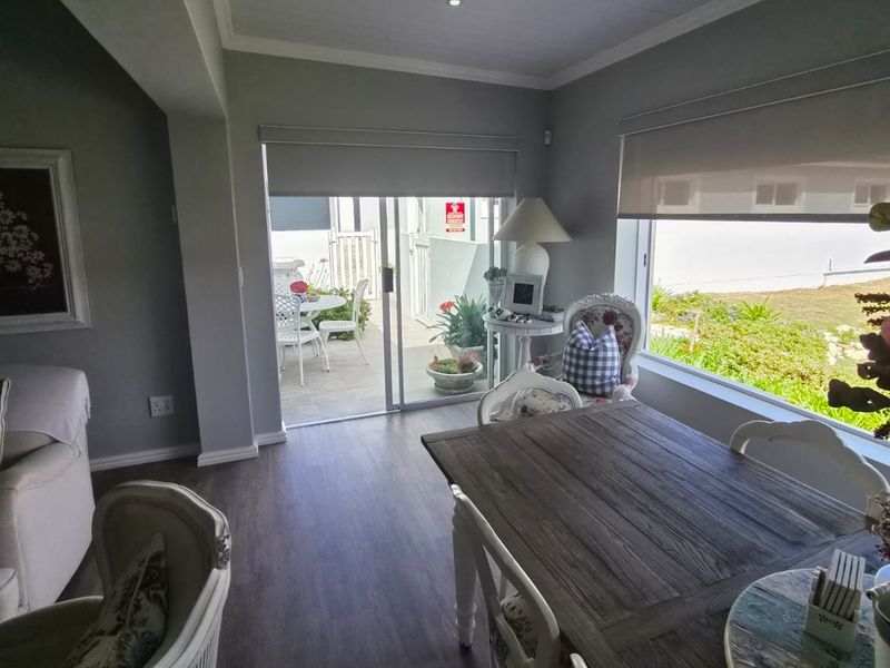 Bright open-plan living and dining area featuring modern laminate flooring, recessed lighting, and large windows with direct access to an outdoor patio space.