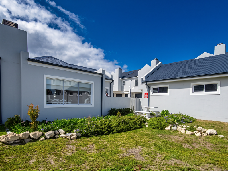 Rear view of the apartment complex featuring a private garden area, concrete patio, and well-maintained grey exterior walls with modern sliding windows.