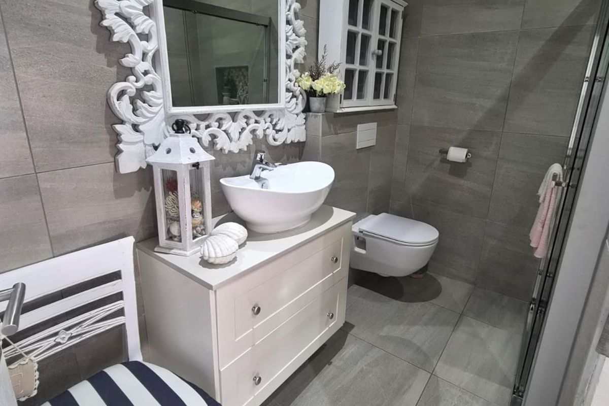 Modern bathroom featuring a wall-mounted toilet, vessel sink with vanity cabinet, and neutral grey floor-to-ceiling tiling.