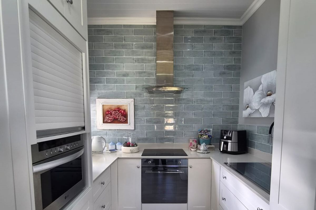 A modern, well-maintained kitchen featuring white shaker cabinetry, stone countertops, a stylish blue subway tile backsplash, and integrated stainless steel appliances.