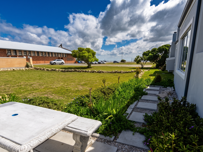 A well-maintained rear garden area featuring a paved walkway, stone garden borders, and a concrete patio space overlooking an open lawn.