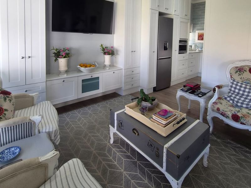 A bright open-plan living area featuring custom white built-in cabinetry, integrated kitchen appliances, and modern laminate flooring, creating a cohesive and functional living space.