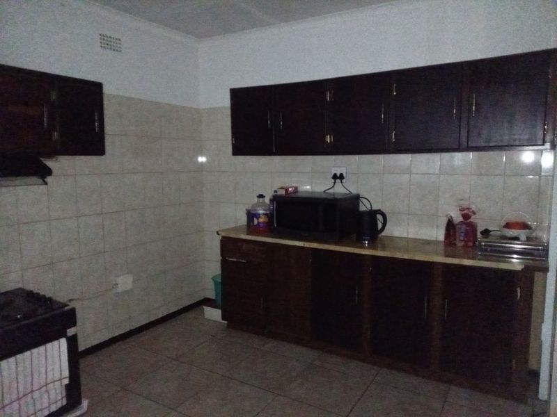 A functional kitchen featuring dark wood cabinetry, tiled backsplash, and tiled flooring, offering a dated aesthetic that could benefit from modern updates.