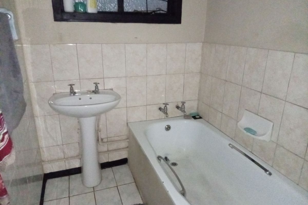 A functional bathroom featuring a pedestal basin, built-in bathtub, and tiled wall finishes. The space is dated and would benefit from modern updates.