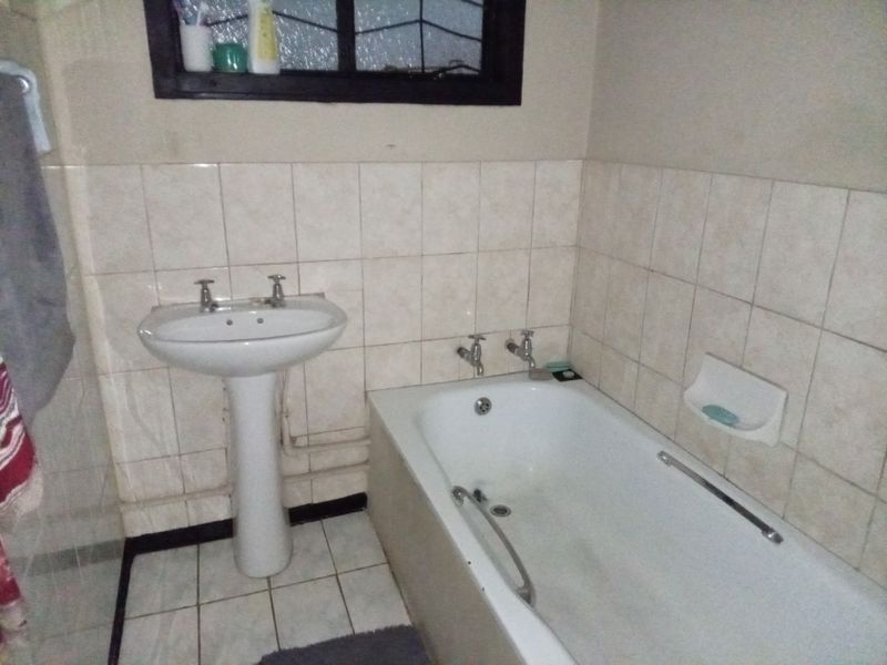 A functional bathroom featuring a pedestal basin, built-in bathtub, and tiled wall finishes. The space is dated and would benefit from modern updates.