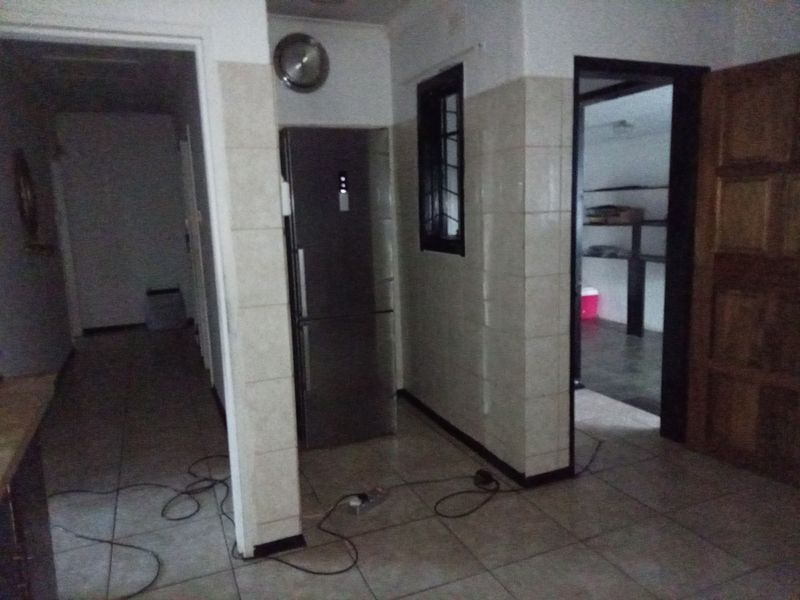 A dimly lit kitchen area featuring tiled walls and flooring, with a doorway leading to an adjacent utility or storage space.