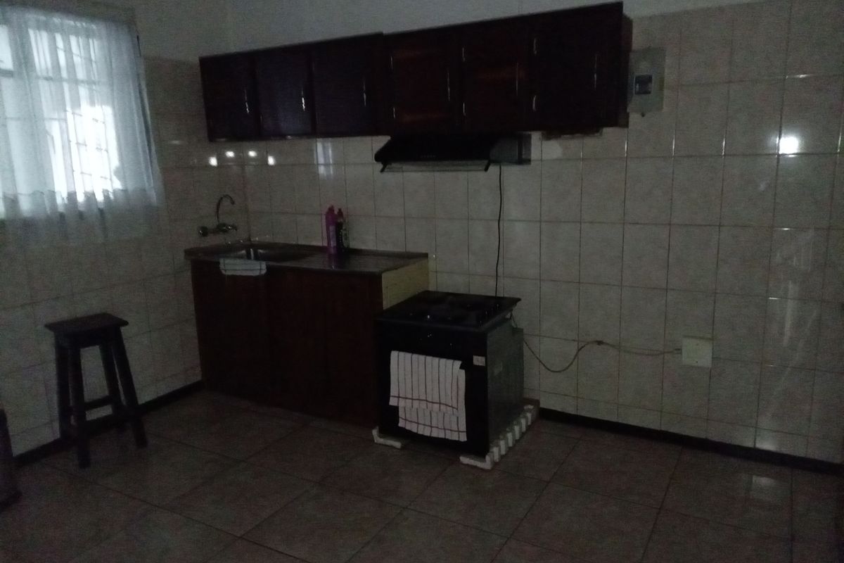 A functional kitchen featuring tiled walls and flooring, dark wood cabinetry, a built-in sink, and an extractor fan.