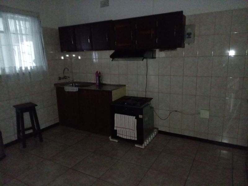 A functional kitchen featuring tiled walls and flooring, dark wood cabinetry, a built-in sink, and an extractor fan.