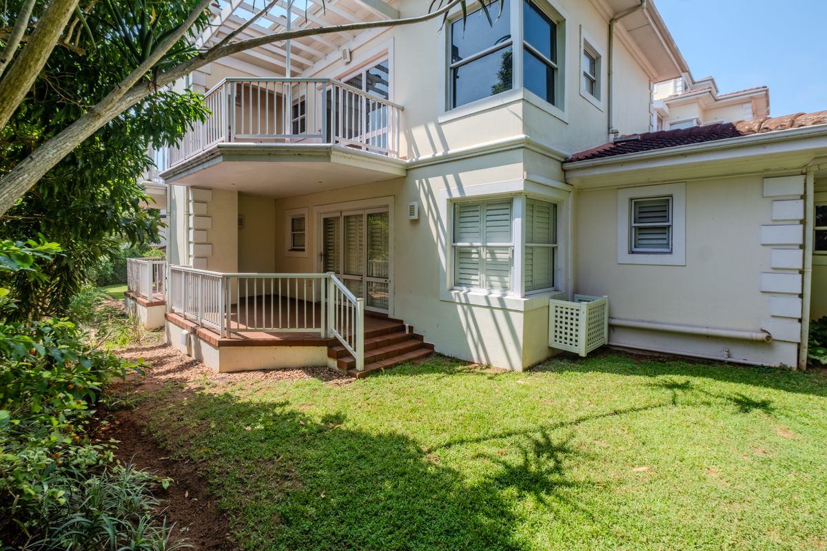 Rear view of the apartment featuring a covered patio, an upper-level balcony with railings, and a private garden area.