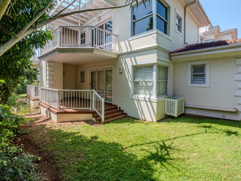Rear view of the apartment featuring a covered patio, an upper-level balcony with railings, and a private garden area.