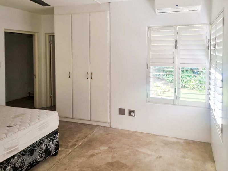 A bedroom featuring built-in cupboards, air conditioning, and plantation shutters, with concrete flooring throughout.