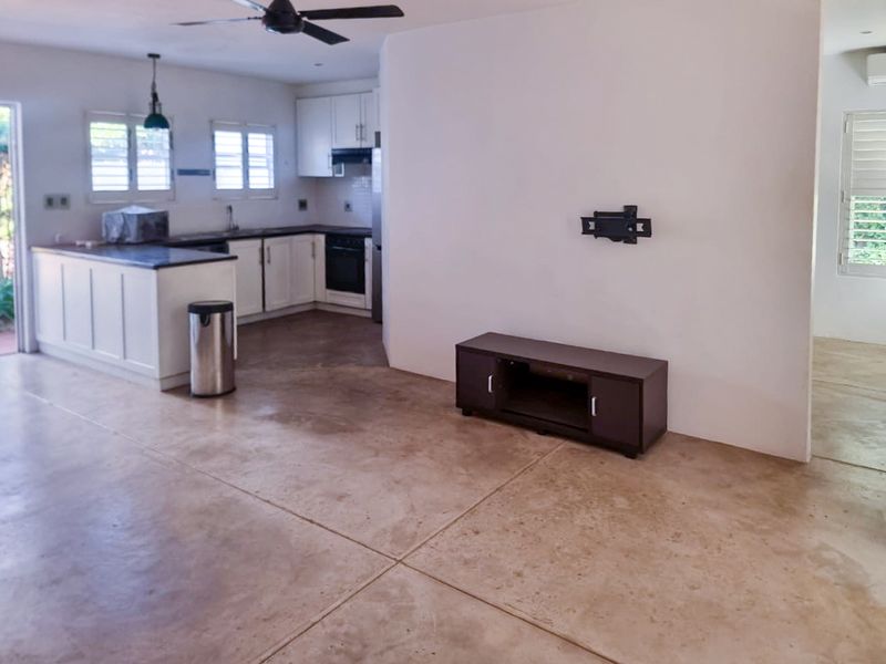 Open plan living and kitchen area featuring polished concrete floors, white cabinetry, built-in oven, and ceiling fan, offering a functional and versatile living space.