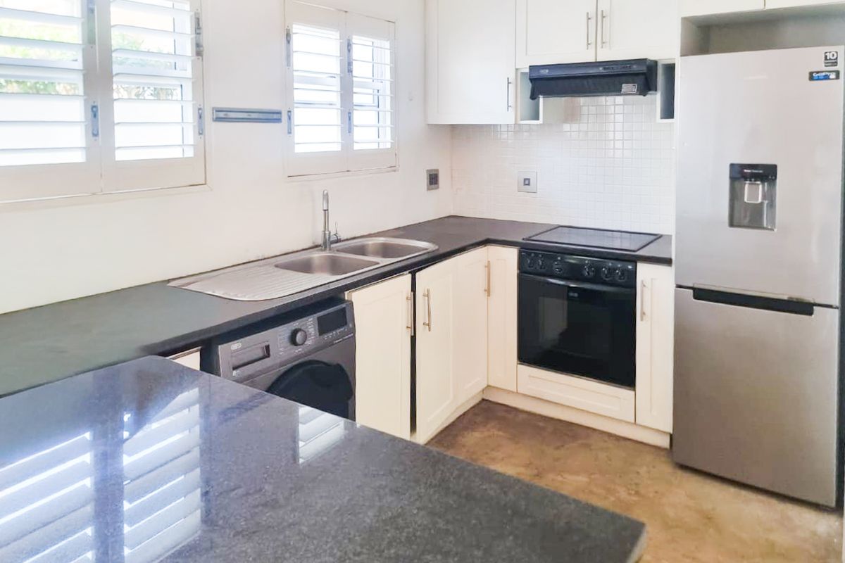 A functional kitchen featuring white cabinetry, granite countertops, a double basin sink, and built-in appliances including an oven and extractor fan.