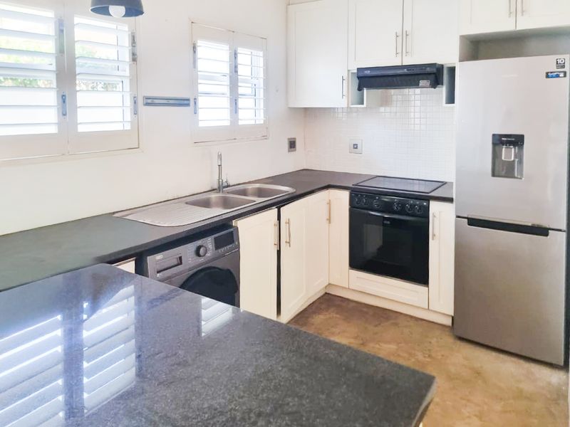 A functional kitchen featuring white cabinetry, granite countertops, a double basin sink, and built-in appliances including an oven and extractor fan.