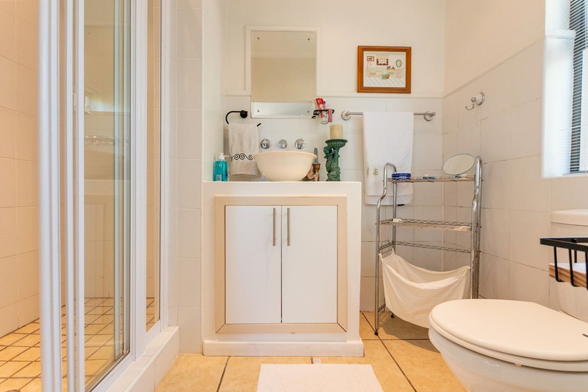 A functional bathroom featuring a shower enclosure, a vanity with a vessel sink, and a toilet, finished with neutral wall and floor tiles.