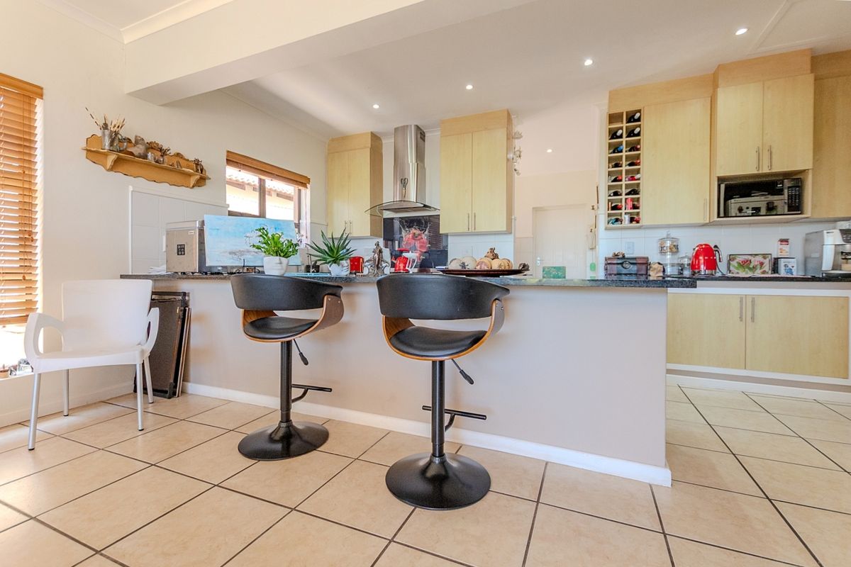 A functional kitchen featuring light wood cabinetry, a stone-topped island with breakfast bar seating, and tiled flooring with recessed lighting.