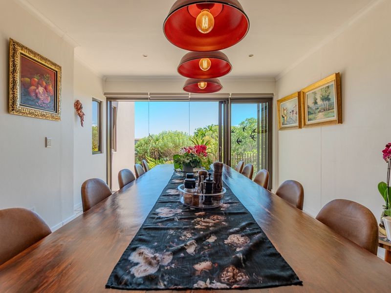 A well-lit dining room featuring large sliding glass doors that open to an outdoor area, complemented by modern pendant lighting and coved ceilings.
