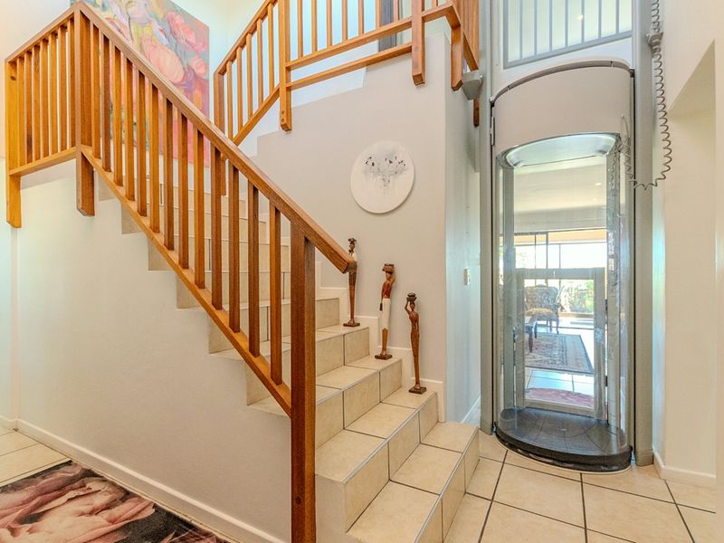 Entrance foyer featuring a tiled staircase with wooden balustrade and a modern glass residential elevator.