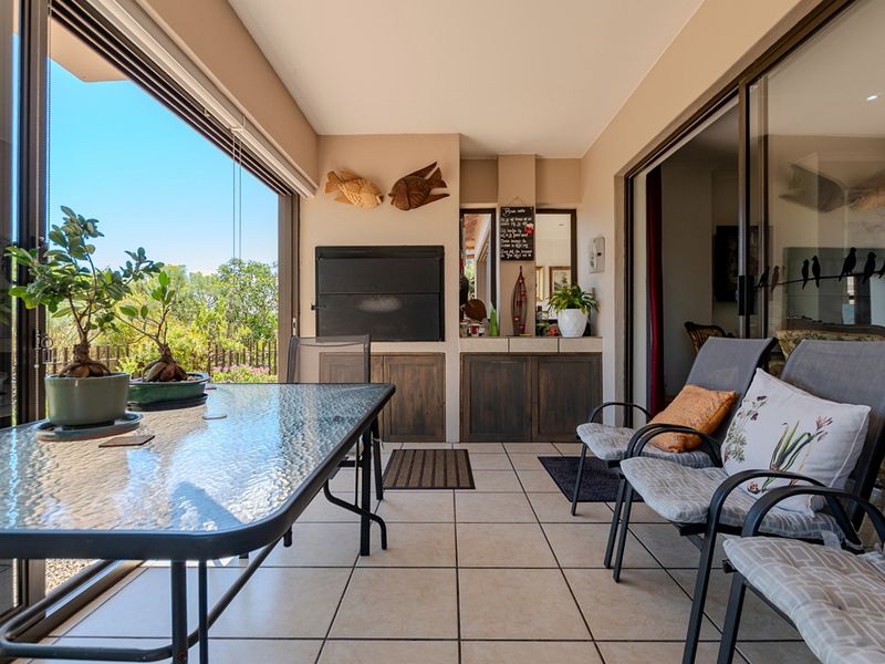 A covered patio area featuring tiled flooring, a built-in braai, and sliding glass doors that open to the garden.