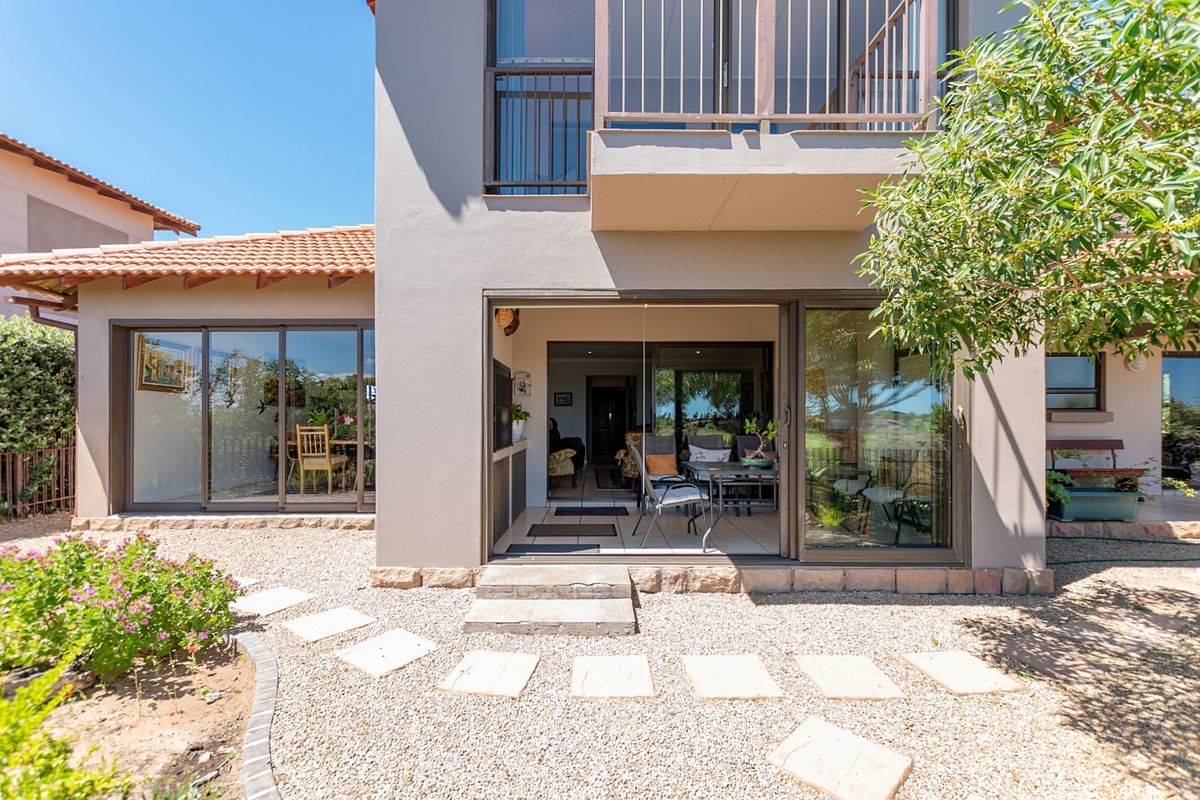 Rear view of the property featuring a gravel garden, stone stepping stones, sliding glass doors leading to the interior, and an upper-level balcony.