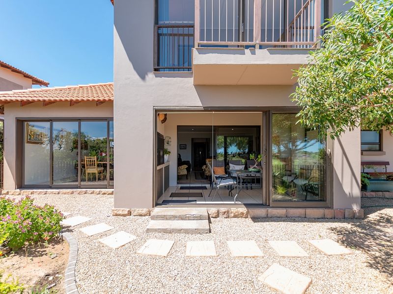 Rear view of the property featuring a gravel garden, stone stepping stones, sliding glass doors leading to the interior, and an upper-level balcony.