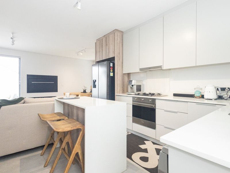 Modern open-plan kitchen featuring sleek white cabinetry, stone countertops, integrated appliances, and a functional breakfast bar island, seamlessly connecting to the living area.
