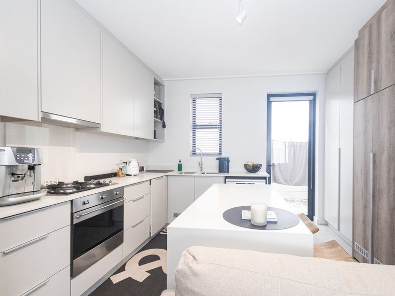 Modern kitchen featuring sleek handleless cabinetry, a central island, gas hob, integrated oven, and direct access to an outdoor area.