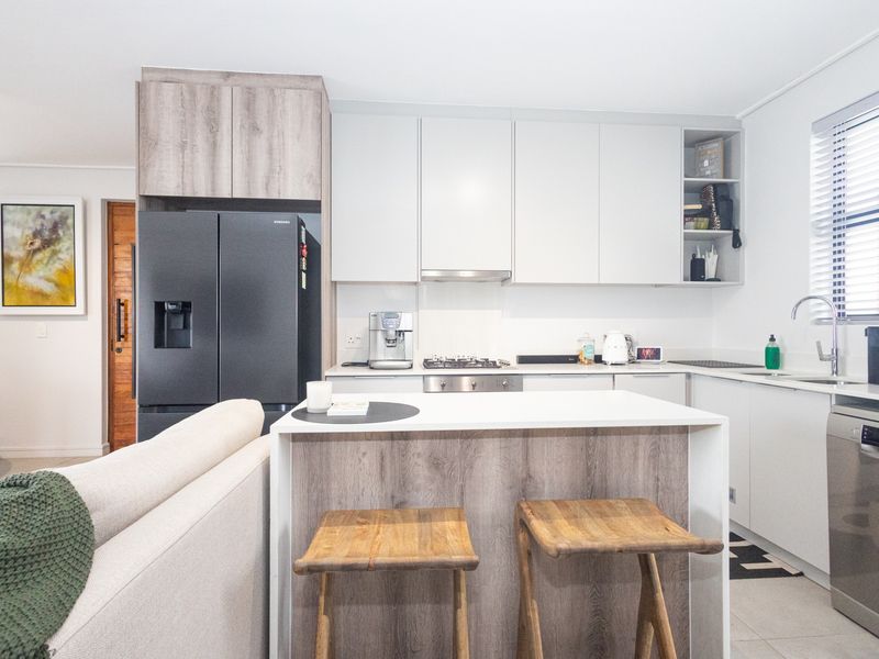 Modern open-plan kitchen featuring sleek white cabinetry, wood-grain accents, a functional island, and integrated appliances, seamlessly connecting to the living area.