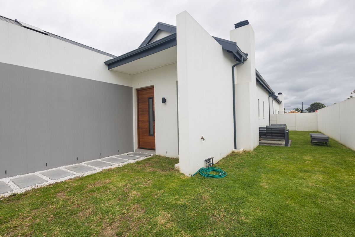A view of the rear exterior featuring a modern timber entrance door, paved walkway, and a well-maintained lawn enclosed by a boundary wall.
