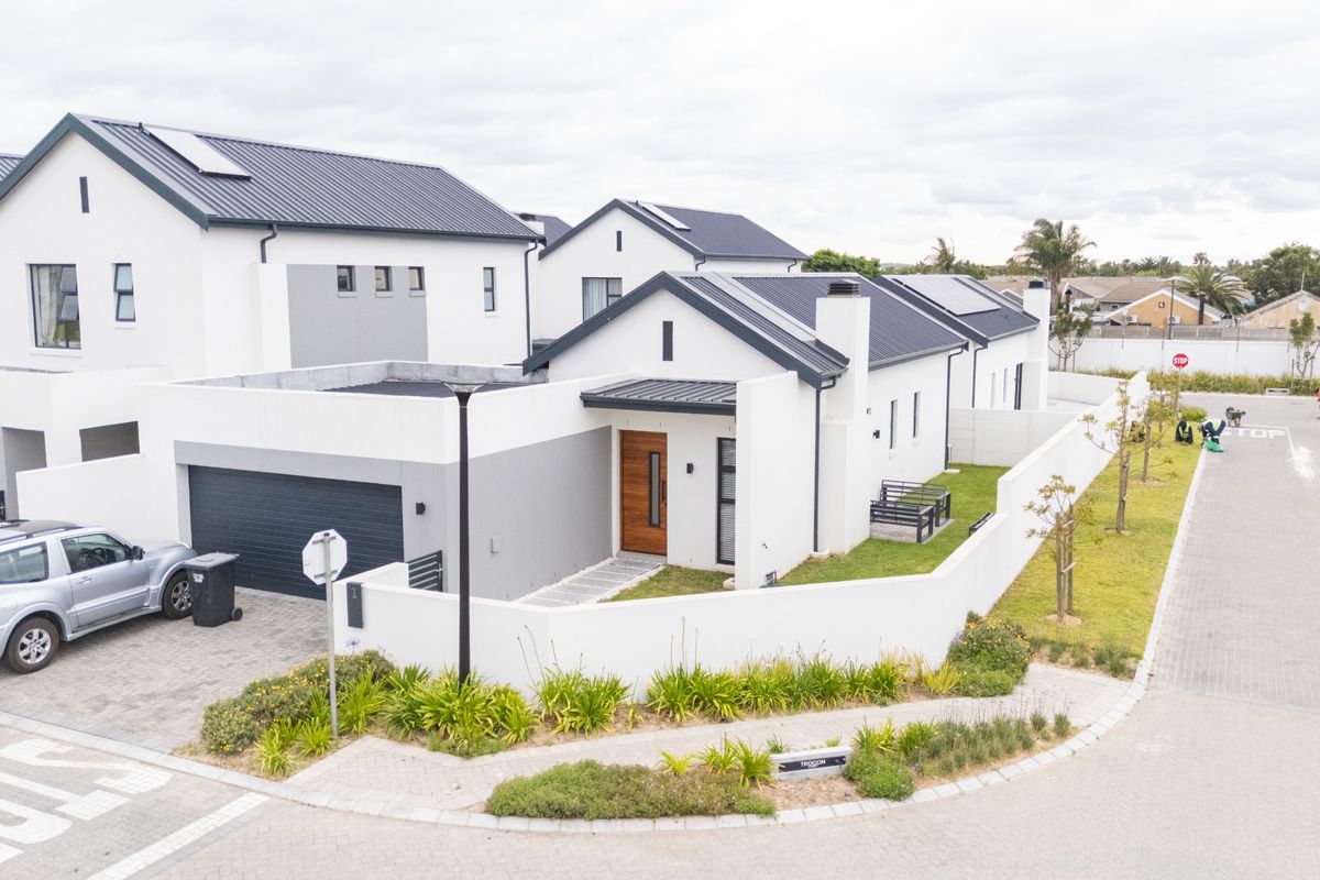 Aerial view of a modern residential property featuring a metal roof, solar panels, paved driveway, and a secure boundary wall.
