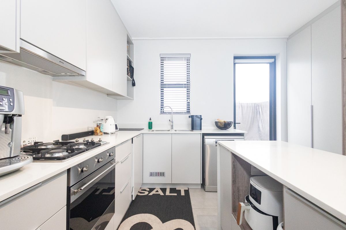 Modern kitchen featuring sleek white cabinetry, stone countertops, integrated appliances, a gas hob, and a functional layout with direct access to the exterior.