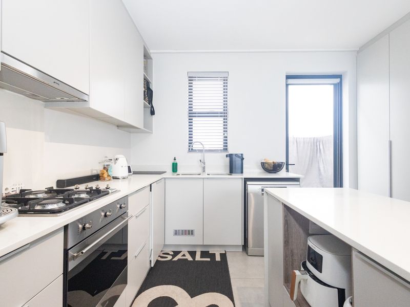 Modern kitchen featuring sleek white cabinetry, stone countertops, integrated appliances, a gas hob, and a functional layout with direct access to the exterior.