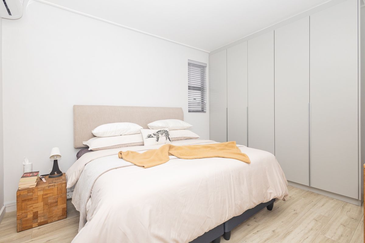 A well-maintained bedroom featuring neutral tones, light laminate flooring, and extensive floor-to-ceiling built-in cupboards for ample storage.