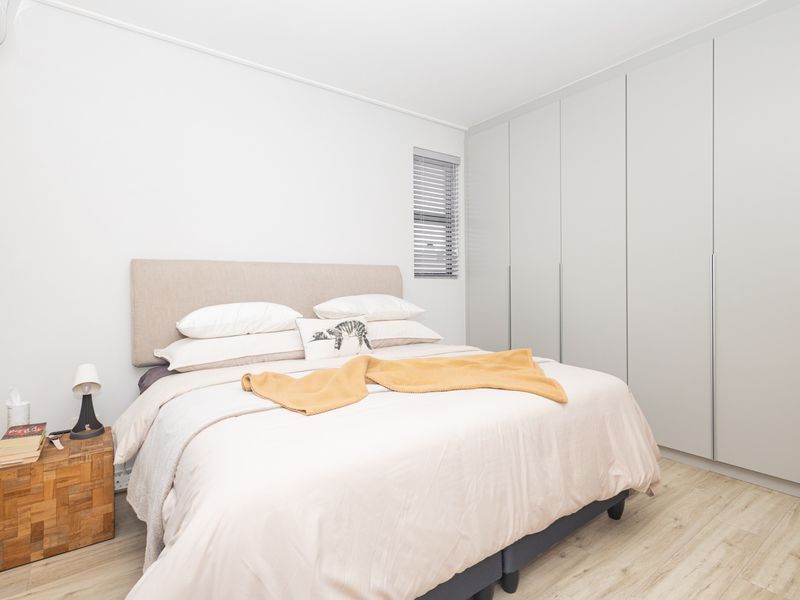 A well-maintained bedroom featuring neutral tones, light laminate flooring, and extensive floor-to-ceiling built-in cupboards for ample storage.