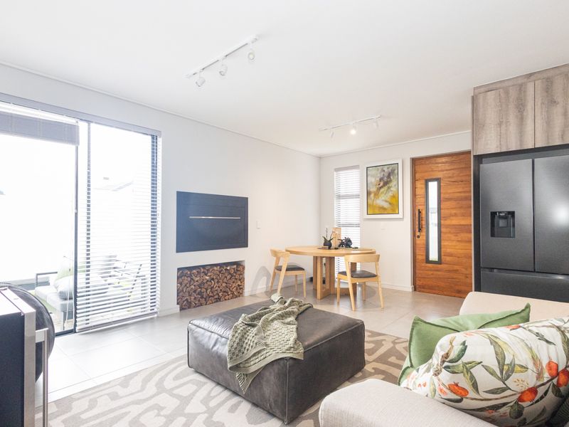 Modern open-plan living area featuring tiled floors, a built-in fireplace with wood storage, track lighting, and direct access to an outdoor patio.