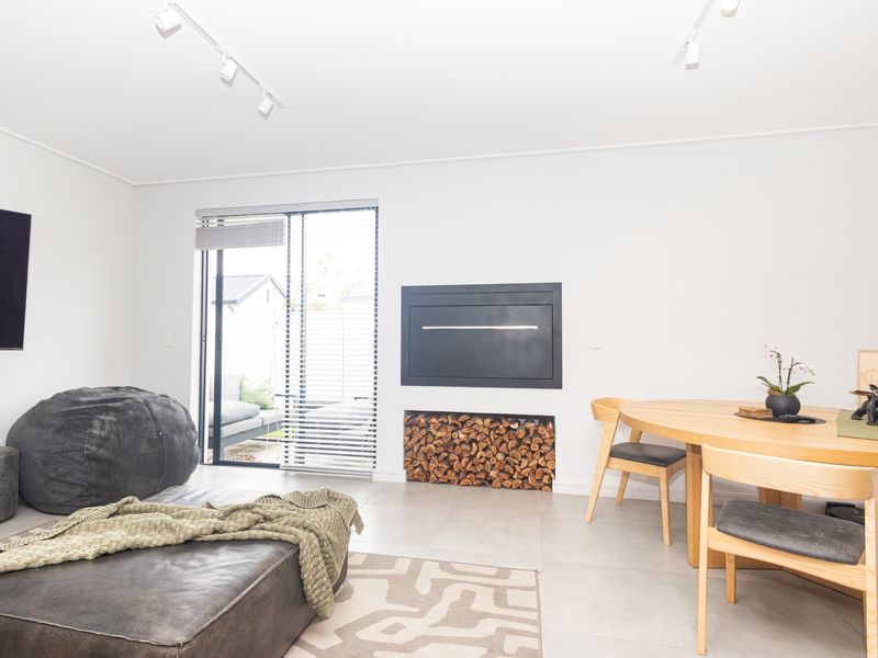 Bright open-plan living and dining area featuring a modern built-in fireplace with integrated wood storage and direct access to an outdoor patio.