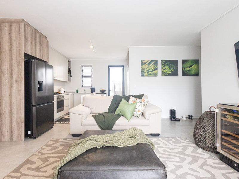 Modern open-plan living area featuring a sleek kitchen with built-in cabinetry, integrated appliances, and neutral tiled flooring throughout the space.
