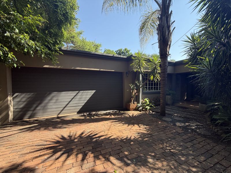 Front exterior view featuring a paved brick driveway, a secure garage door, and established garden landscaping leading to the home entrance.