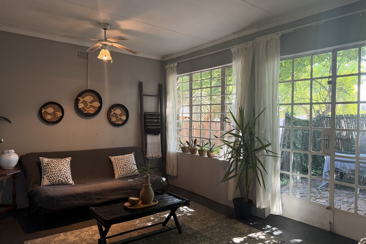A cozy living room featuring a ceiling fan, steel-framed windows, and french doors that provide natural light and access to the garden area.