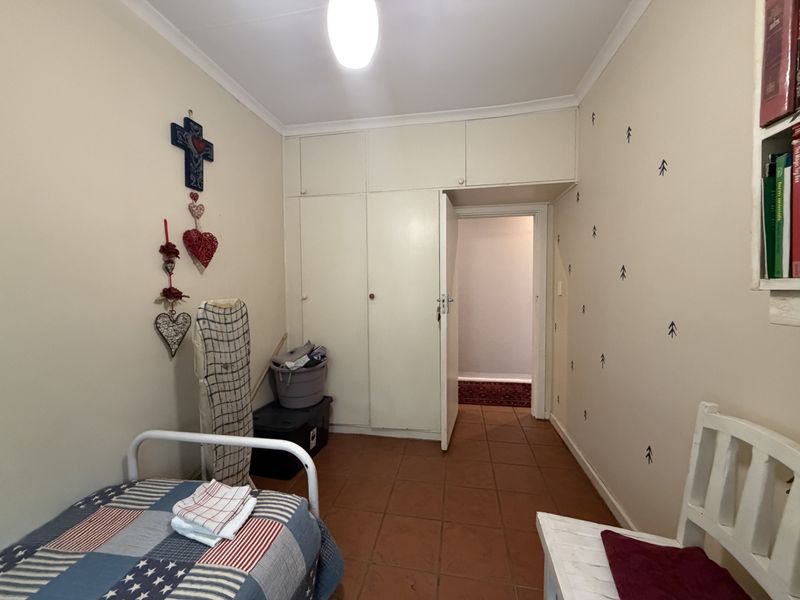 A functional bedroom featuring built-in cupboards, tiled flooring, and coved ceilings, offering a practical space with potential for cosmetic updates.