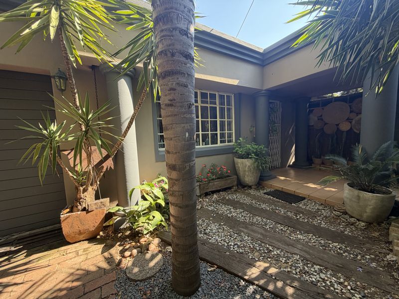 A charming covered patio area featuring tiled flooring, decorative columns, and secure window access, offering a pleasant outdoor space for relaxation.