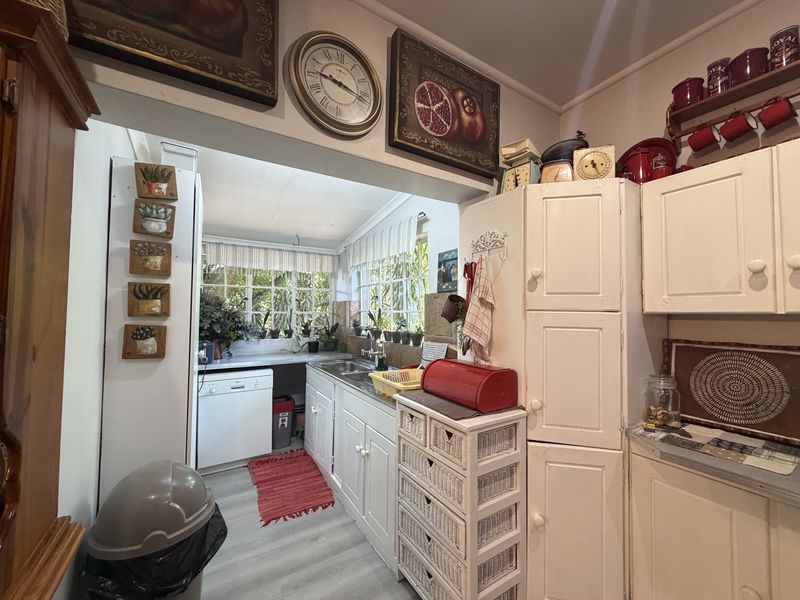 A functional scullery or secondary kitchen area featuring built-in white cabinetry, a stainless steel sink, and large windows providing natural light.