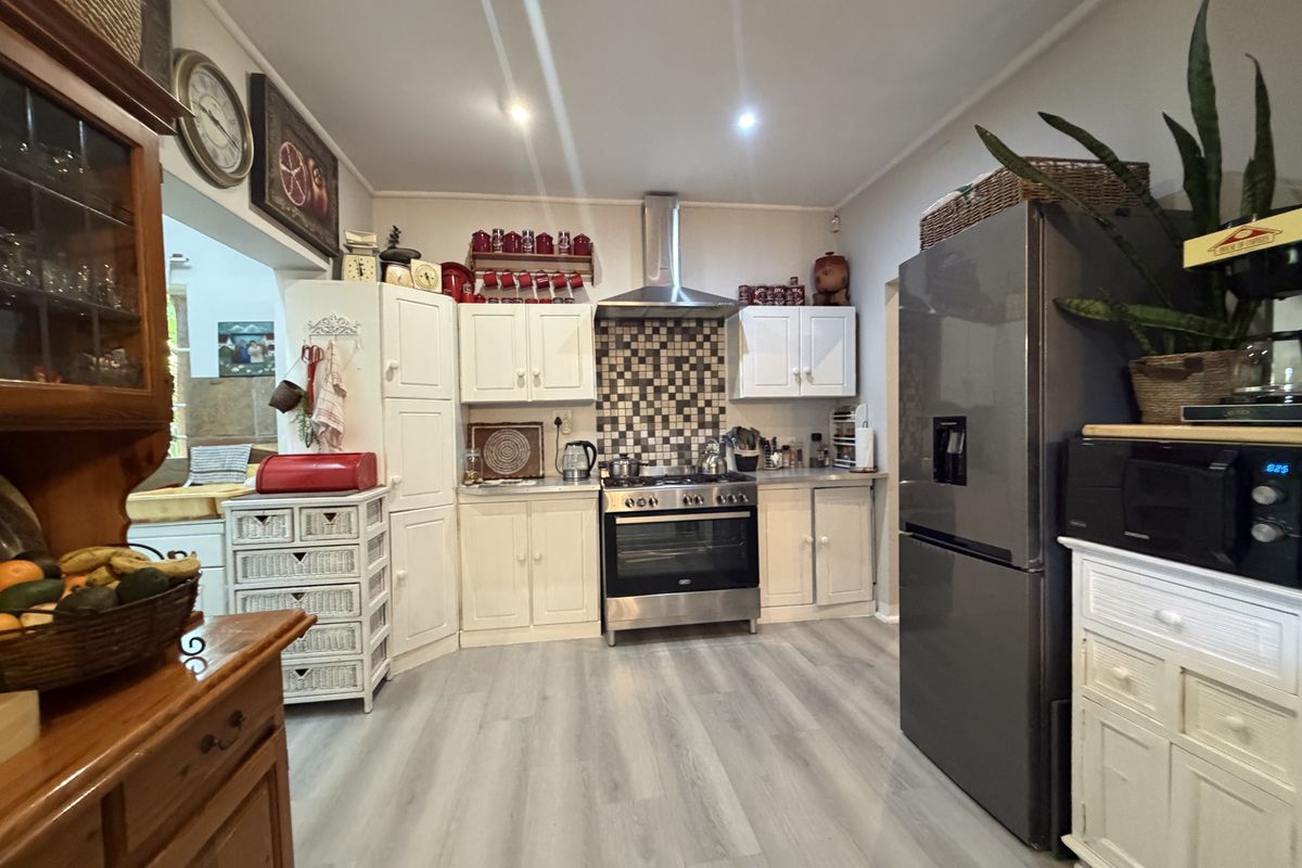 A functional kitchen featuring white cabinetry, a stainless steel oven with extractor fan, mosaic tile splashback, and modern laminate flooring.